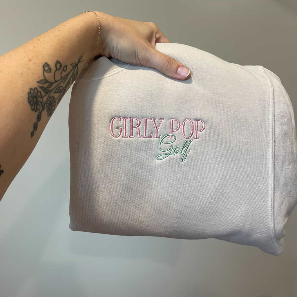 White bag with 'GIRLY POP Golf' text held by a hand on a neutral background