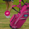 Pink golf bag with a woman in a black skirt on a golf course