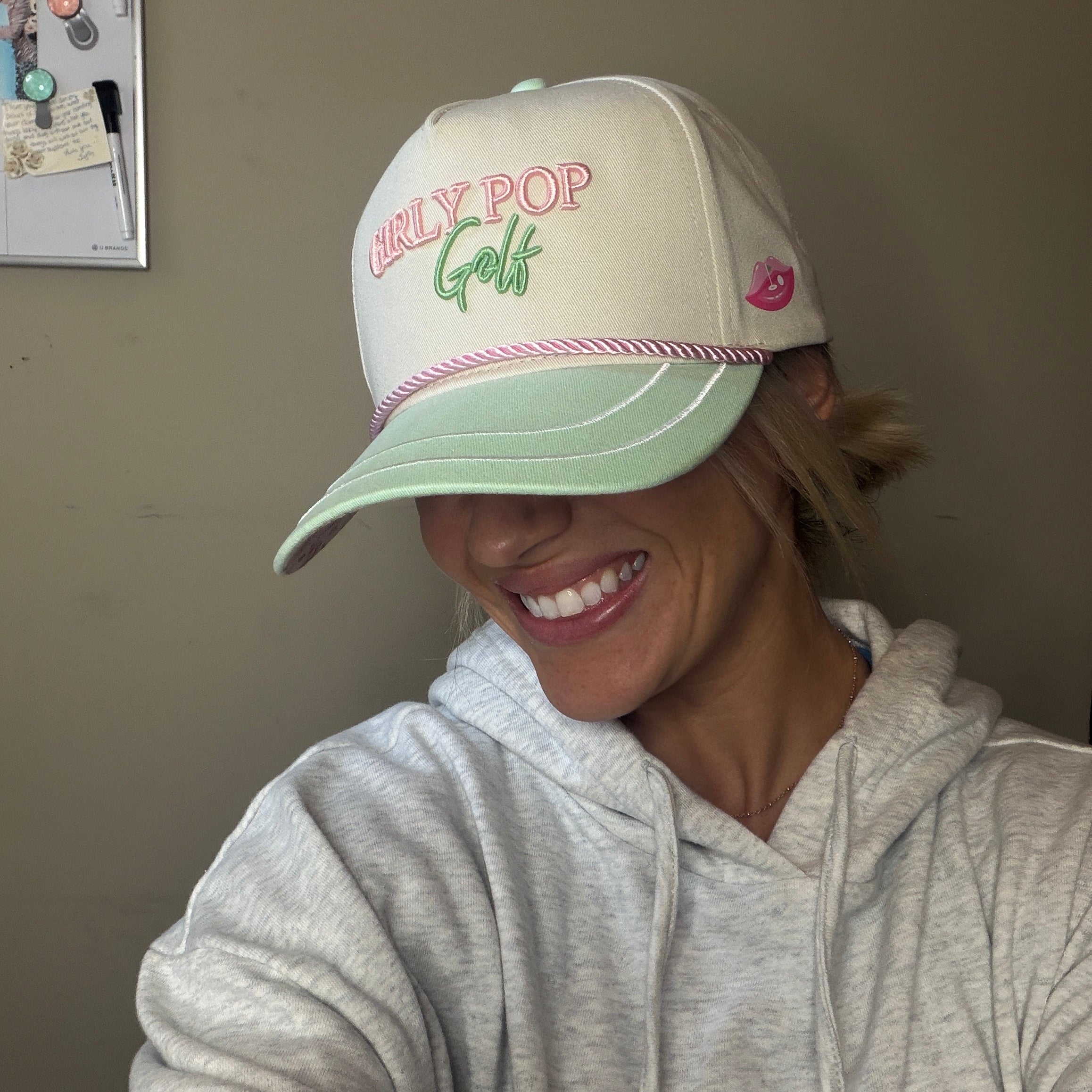Person wearing a cap with 'Early Pop Golf' text, smiling indoors.