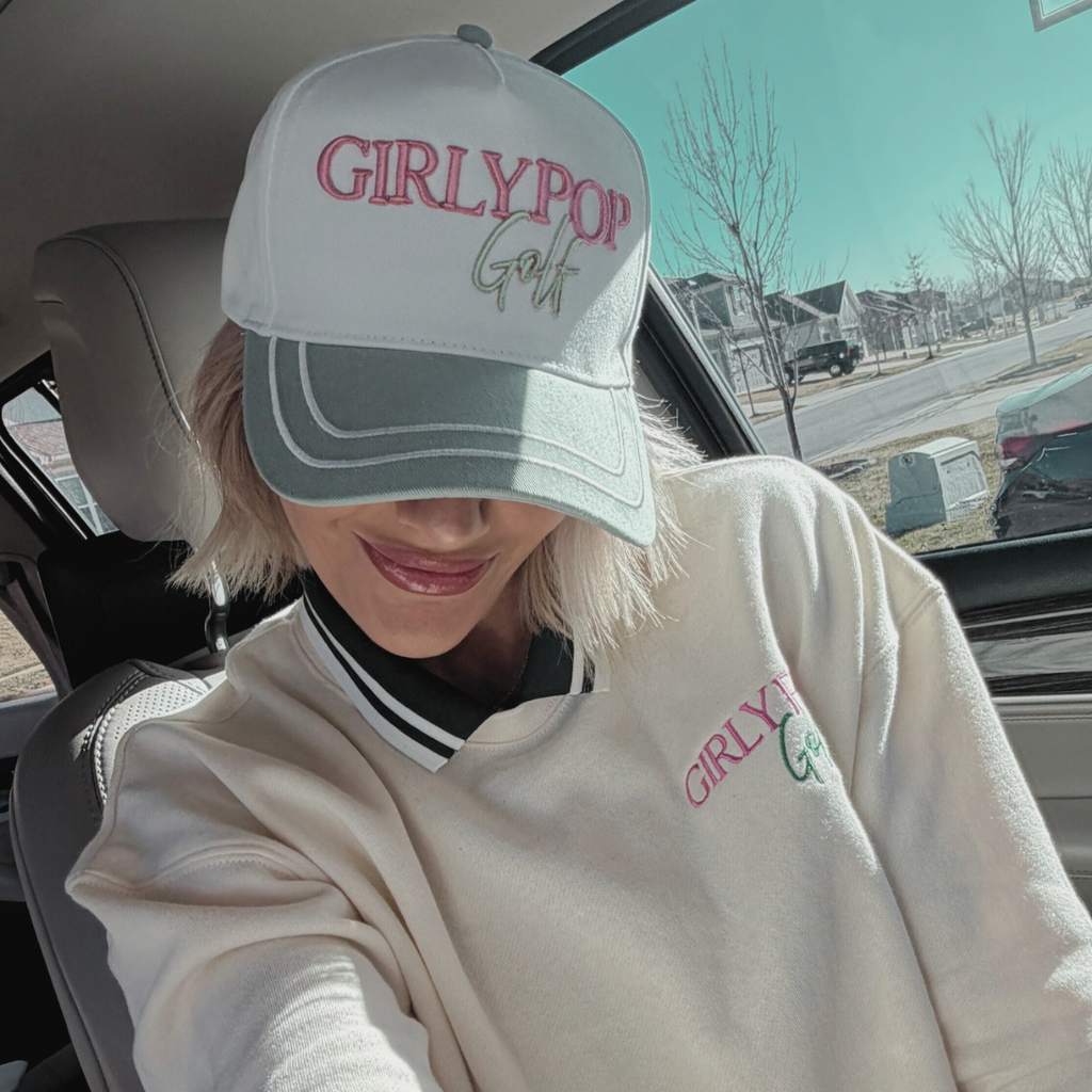 Person wearing a 'GIRLY POP' cap and sweatshirt inside a vehicle.